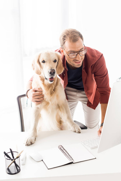 businessman hugging golden retriever while working in modern office  - Photo, Image
