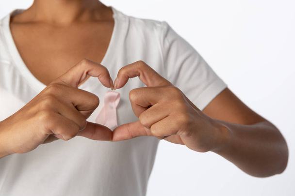 Woman making heart with their fingers around pink ribbon on a white background - Фото, зображення