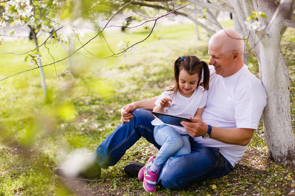 Großvater umarmt Enkelin mit digitalem Tablet im grünen Park. - Foto, Bild