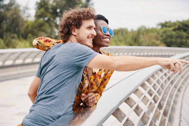 multiracial couple standing on bridge road, man pointing finger on way  - Фото, изображение