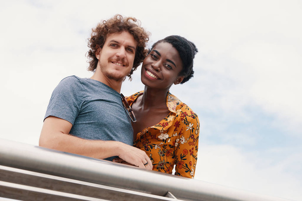 couple multiracial en tenues décontractées debout à la clôture sous les nuages en regardant la caméra
 - Photo, image