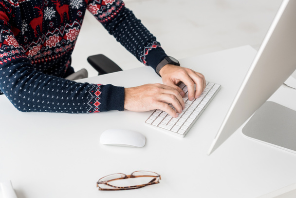 cropped view of businessman in christmas sweater printing on keyboard in modern office - Photo, Image