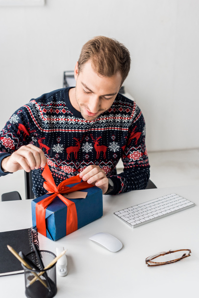 smiling businessman in christmas sweater opening gift box  - Foto, Bild
