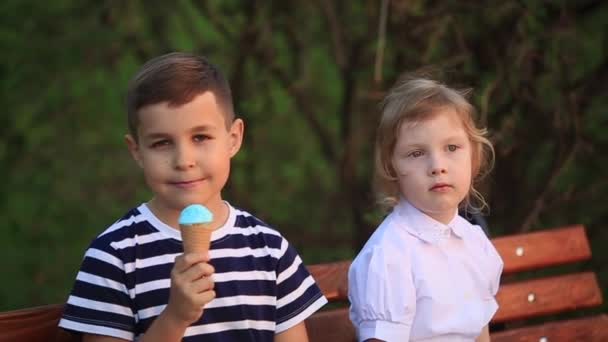 Niño comiendo un helado y sentado en el banco mientras que la chica está buscando
 - Metraje, vídeo