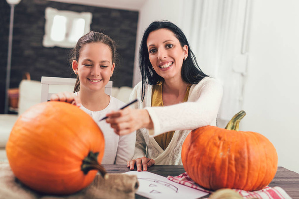 Mother with daughter creating big orange pumpkin for Halloween and having fun - Фото, зображення