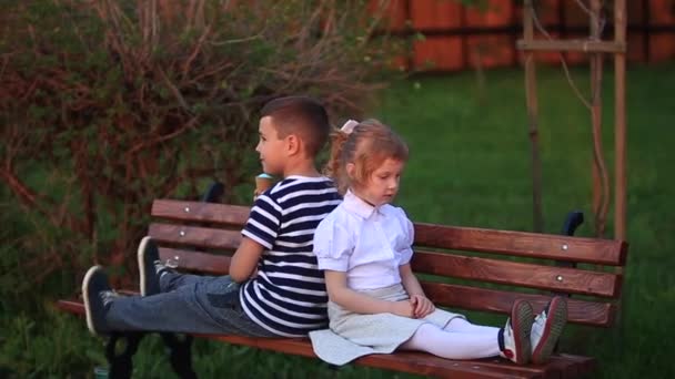 Мальчик ест мороженое и сидит на скамейке, пока девушка смотрит
 - Кадры, видео