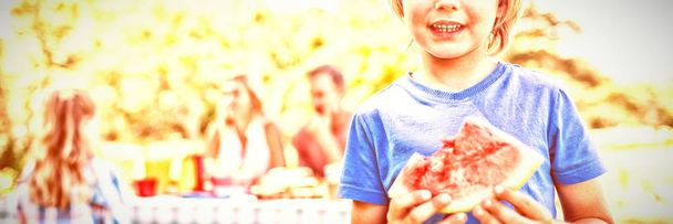 Portrait of smiling boy holding watermelon in the park - Zdjęcie, obraz