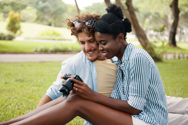 couple multiracial assis sur la prairie dans le parc et en regardant les photos de la caméra
  - Photo, image