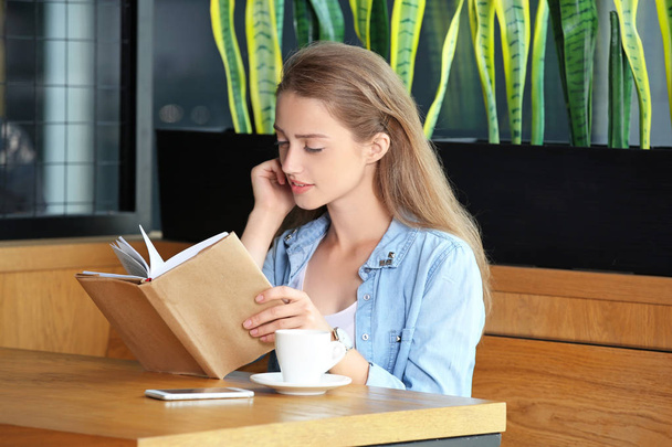 Młoda kobieta czyta książkę w kawiarni - Zdjęcie, obraz