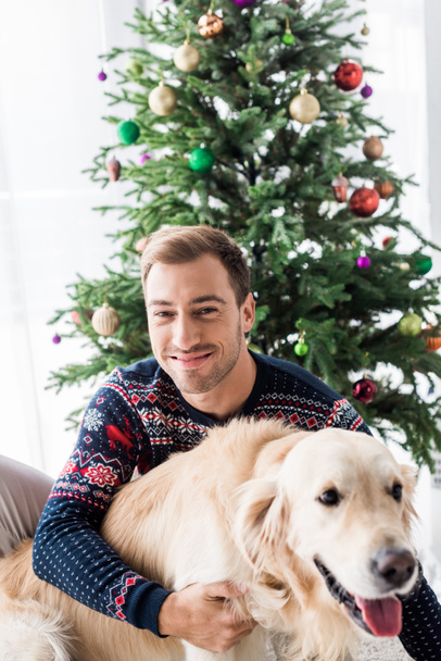 smiling man in christmas sweater hugging golden retriever dog   - Photo, image