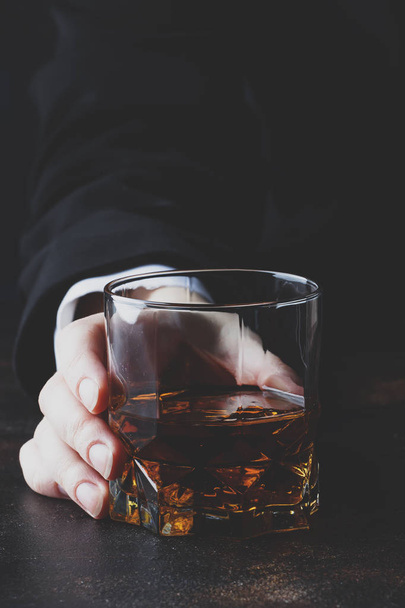 Whiskey glass in hand on the dark bar counter, selective focus - Фото, зображення