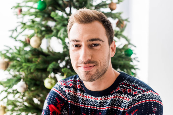 man in christmas sweater against christmas tree  - Foto, imagen