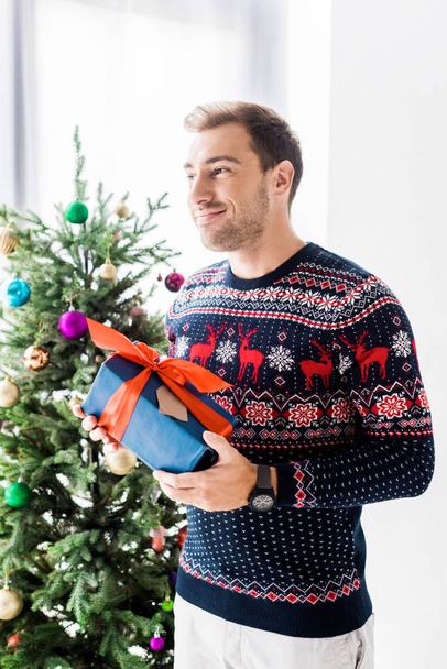 Lächelnder Mann im Weihnachtspullover mit Geschenkbox  - Foto, Bild