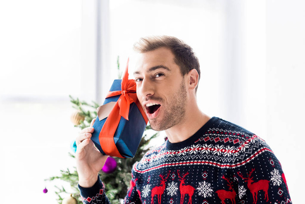 man in christmas sweater with gift box near head  - Foto, Bild