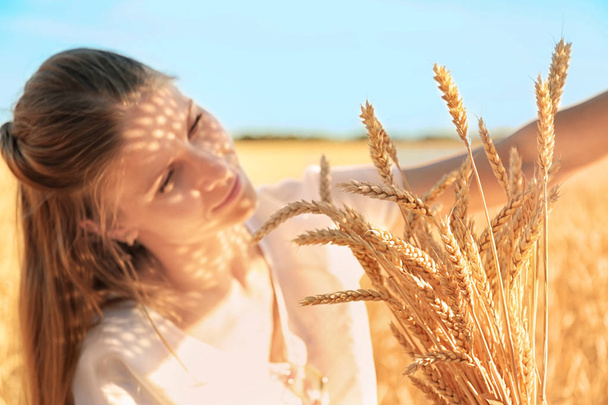 Beautiful woman with wheat spikelets in field on sunny day - Fotografie, Obrázek