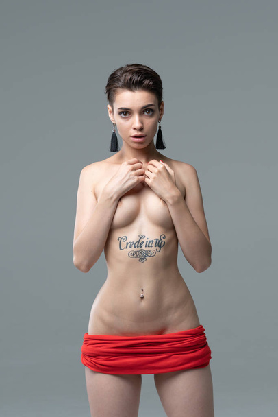 retrato de una joven hermosa chica desnuda en el estudio, de pie en una falda roja
 - Foto, Imagen