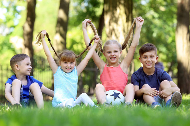 Słodkie dzieci siedzi na zielonej trawie w parku - Zdjęcie, obraz