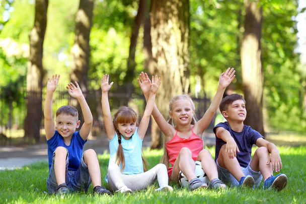 Słodkie dzieci siedzi na zielonej trawie w parku - Zdjęcie, obraz