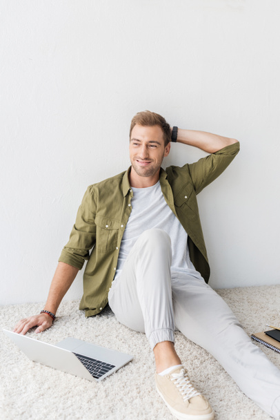 smiling man sitting on beige rug and looking away - Photo, Image