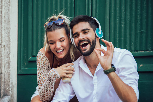 Retrato de belo casal de turistas jovens sorridentes sentados nas escadas usando tablet e ouvir música
. - Foto, Imagem