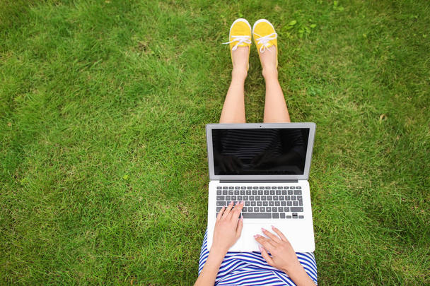 Giovane donna con computer portatile poggiata su erba verde nel parco
 - Foto, immagini