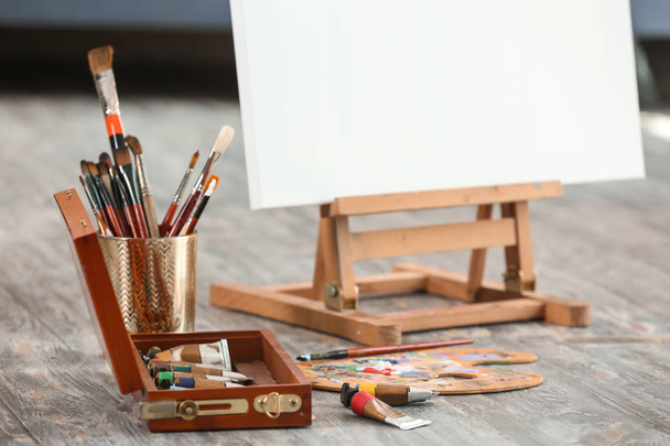 Set of brushes and paints with easel on floor in artist's workshop - 写真・画像