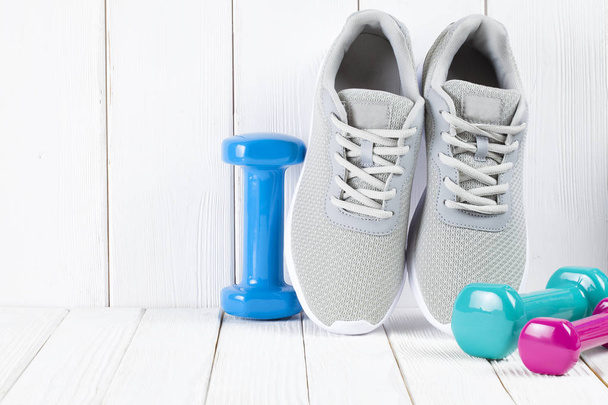 Sport and fitness symbols - sneakers, and colorful dumbbells on wooden wall background - Φωτογραφία, εικόνα