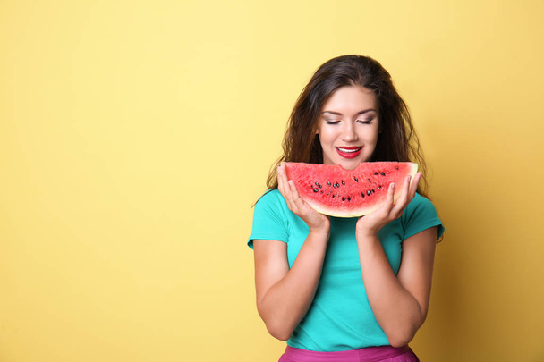 schöne junge Frau mit einer Scheibe leckerer Wassermelone auf farbigem Hintergrund - Foto, Bild