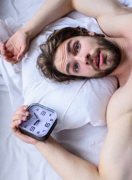 Man unshaven surprised shocked face lay pillow alarm clock top view. Toughest part of morning simply getting out of bed. Guy missed alarm clock ringing. Get up early morning tips. Oversleep problem - 写真・画像
