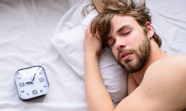 Oversleep problem. Man unshaven sleepy face lay pillow alarm clock top view. Guy sleep missed alarm clock ringing. Manage proper regime tips. Toughest part of morning simply getting out of bed - Foto, Imagen