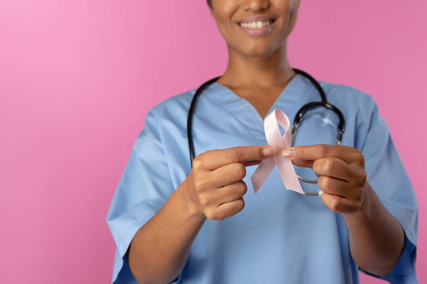 Nurse holding breast cancer awareness pink ribbon with both hands on a pink background - Φωτογραφία, εικόνα