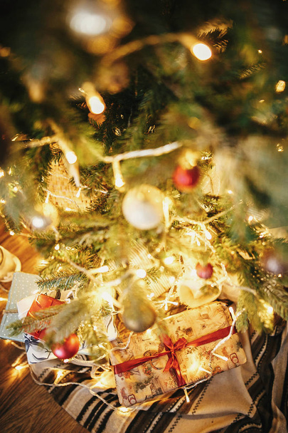 élégantes boîtes cadeaux de Noël sous le bel arbre de Noël avec des ornements, des lumières dorées et des cadeaux dans la salle de fête. boules rouges et dorées sur branches de pins. décor pour les vacances d'hiver
 - Photo, image