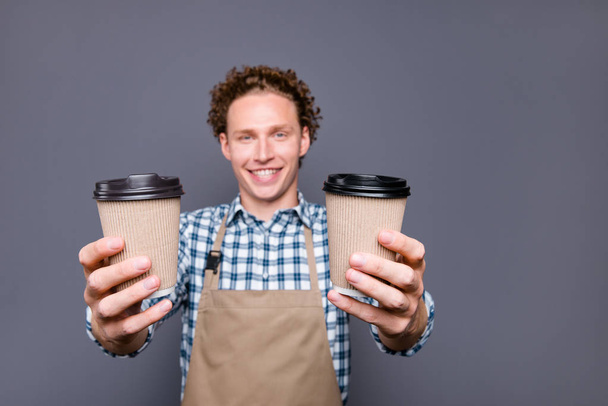 Stylish nice attractive cheerful funny guy with wavy hair in casual checkered shirt, cafe owner, giving two paper cups, offering take-away, rest, pause, relax. Isolated over grey background - Foto, imagen