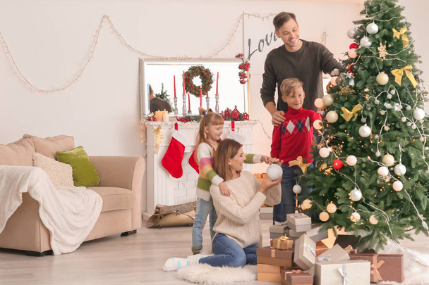 Щаслива сім'я прикрашає ялинку в кімнаті
 - Фото, зображення