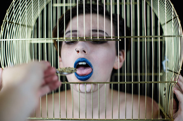 Концептуальний знімок жінки з блакитними губами і кліткою птахів на голові, приймаючи їжу з ложки
  - Фото, зображення