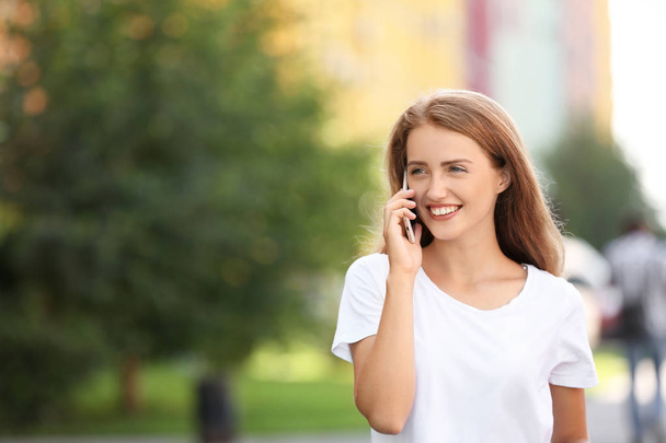 Kaunis nuori nainen puhuu matkapuhelimella kävellessään ulkona
 - Valokuva, kuva