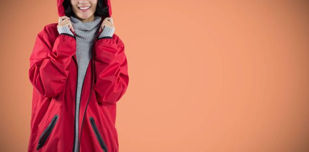 Smiling woman in hooded jacket standing against orange background - Fotografie, Obrázek