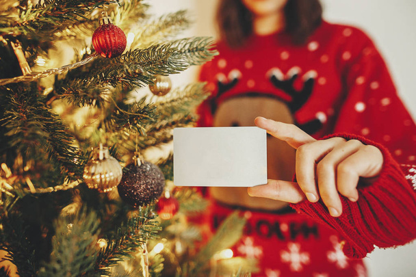 main tenant carte de crédit close-up sur fond de bel arbre de Noël doré avec des lumières dans la salle de fête. Noël shopping et concept de vente. réduction. vendredi noir
 - Photo, image
