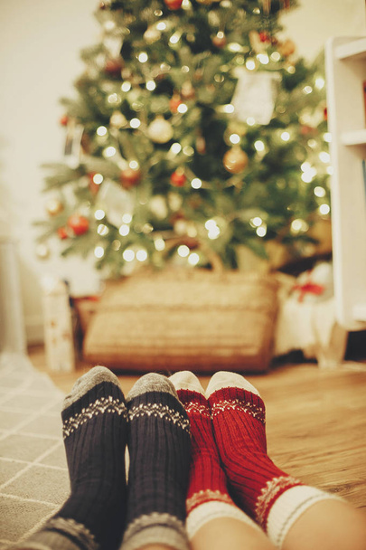 family legs in stylish festive socks on background of golden beautiful christmas tree with lights in festive room. relax time together. cozy winter holidays. warm atmospheric moment - Фото, зображення