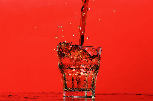 splash of water in glass for whiskey on red background, copy space. - Fotografie, Obrázek