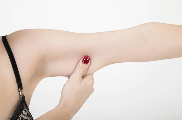 Een vrouwelijke hand overtollig vet van haar arm knijpen over Wit met kopie ruimte - Foto, afbeelding