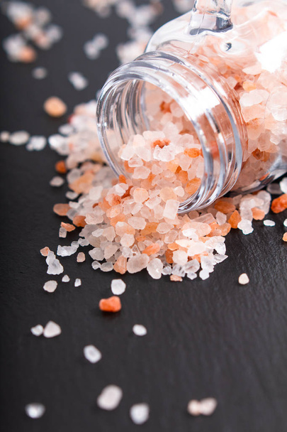 Концепция здорового питания розовая гималайская соль, выливаемая из стеклянной банки на фоне черного камня
 - Фото, изображение
