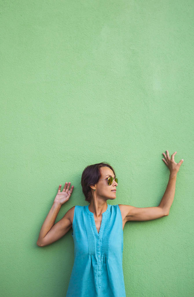 Ragazza sullo sfondo di un muro verde. Una donna snella con gli occhiali posa in una strada della città. Una bella bruna cammina lungo una strada della città
. - Foto, immagini
