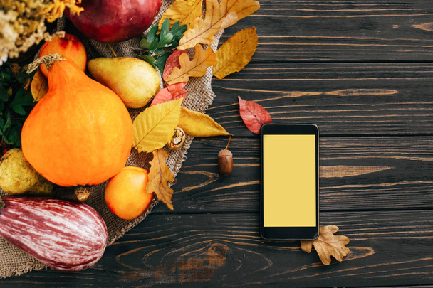 幸せな感謝祭のコンセプトです。木製の素朴なテーブル、フラットに果実を置くと美しい明るい紅葉、どんぐり、ナッツ、かぼちゃの空の画面と電話します。テキストのためのスペース。居心地の良い秋のシーズン. - 写真・画像