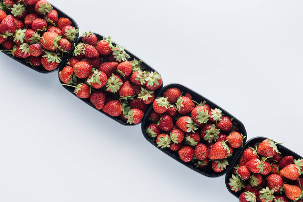 Draufsicht auf Containerreihe mit reifen Erdbeeren auf weißer Oberfläche - Foto, Bild
