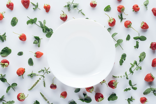 vista superior del plato vacío rodeado de fresas maduras y hojas de menta sobre una mesa blanca
 - Foto, Imagen
