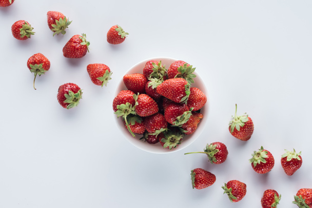 top view of bowl of fresh strawberries on white tabletop - Fotó, kép
