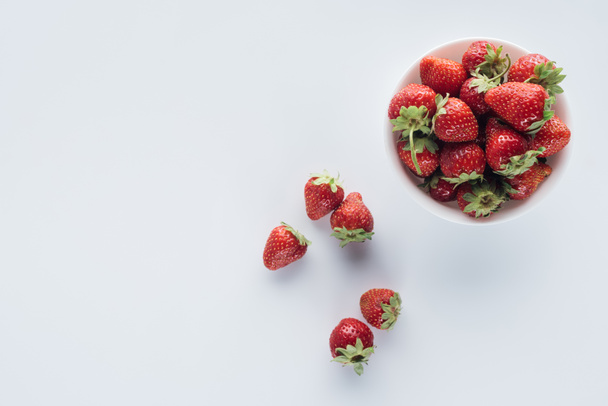 top view of bowl of fresh whole strawberries on white surface - Foto, Imagem