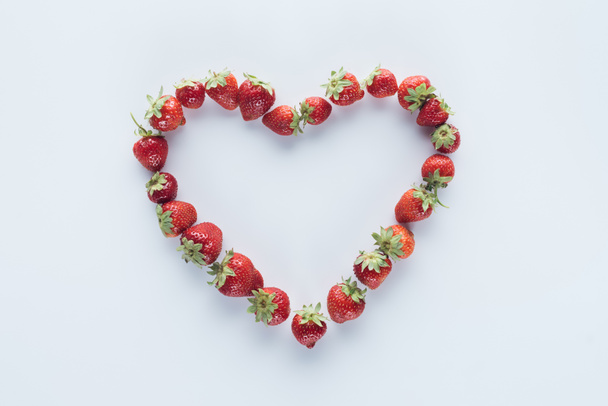 top view of heart shape sign made of fresh strawberries on white surface - Photo, Image