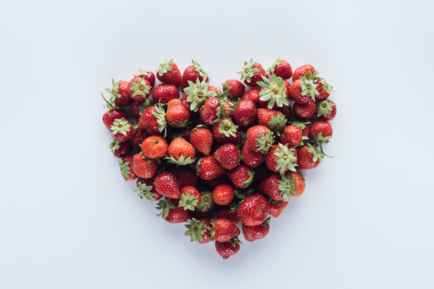 bovenaanzicht van hart vorm teken gemaakt van rijpe aardbeien op witte ondergrond - Foto, afbeelding